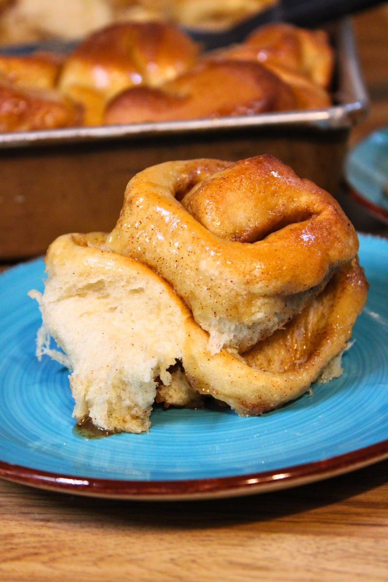 Pan of homemade caramel cinnamon rolls with golden tops and sticky caramel sauce, with individual rolls on turquoise plates on a wooden table.