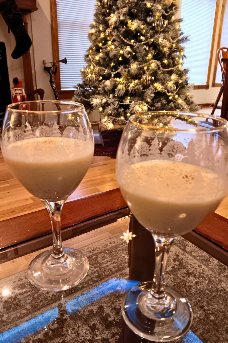 The best homemade eggnog made from scratch on a table with a Christmas tree and fireplace in the background.