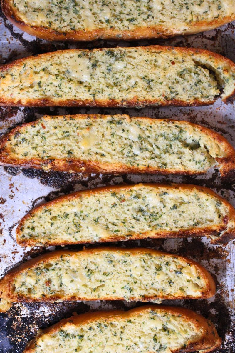 Restaurant style garlic bread with garlic butter spread on it toasted on a baking sheet.