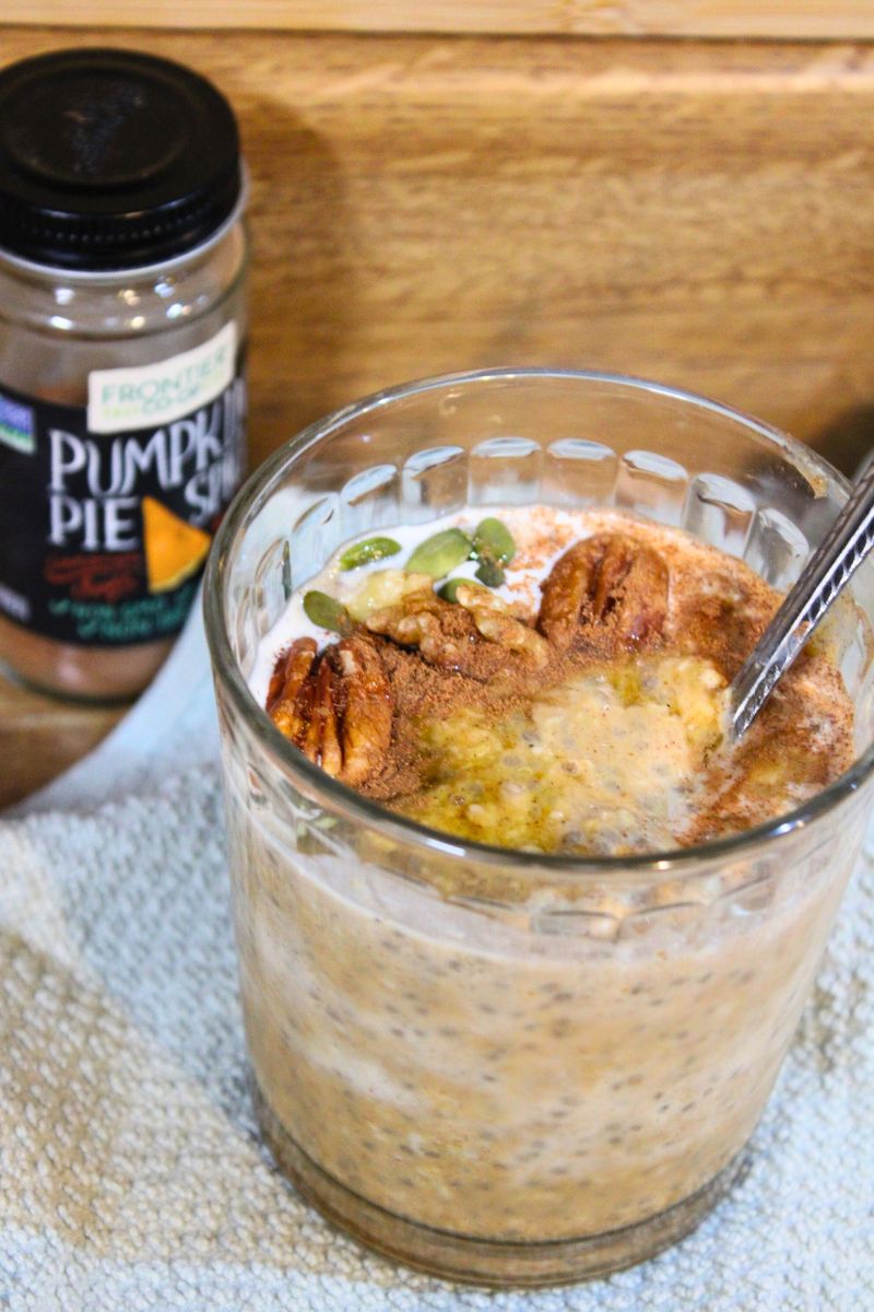 Healthy overnight pumpkin spice oats in a glass jar topped with pecans, pumpkin seeds, and cinnamon, with pumpkin pie spice jar in the background – easy fall breakfast recipe from Santa Rosa Homestead.
