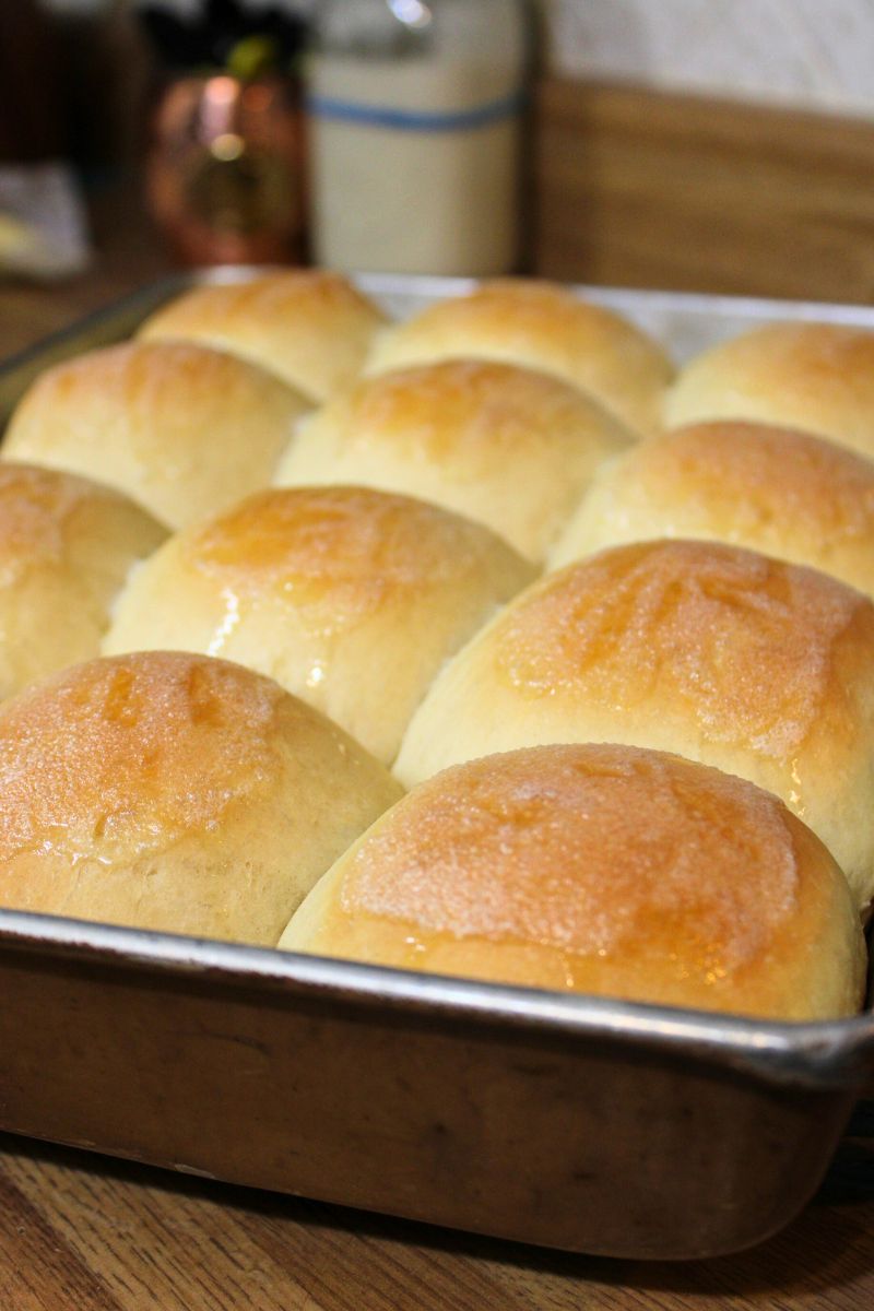 Golden brown homemade dinner rolls fresh from the oven in a baking pan, brushed with butter for a soft and fluffy texture.