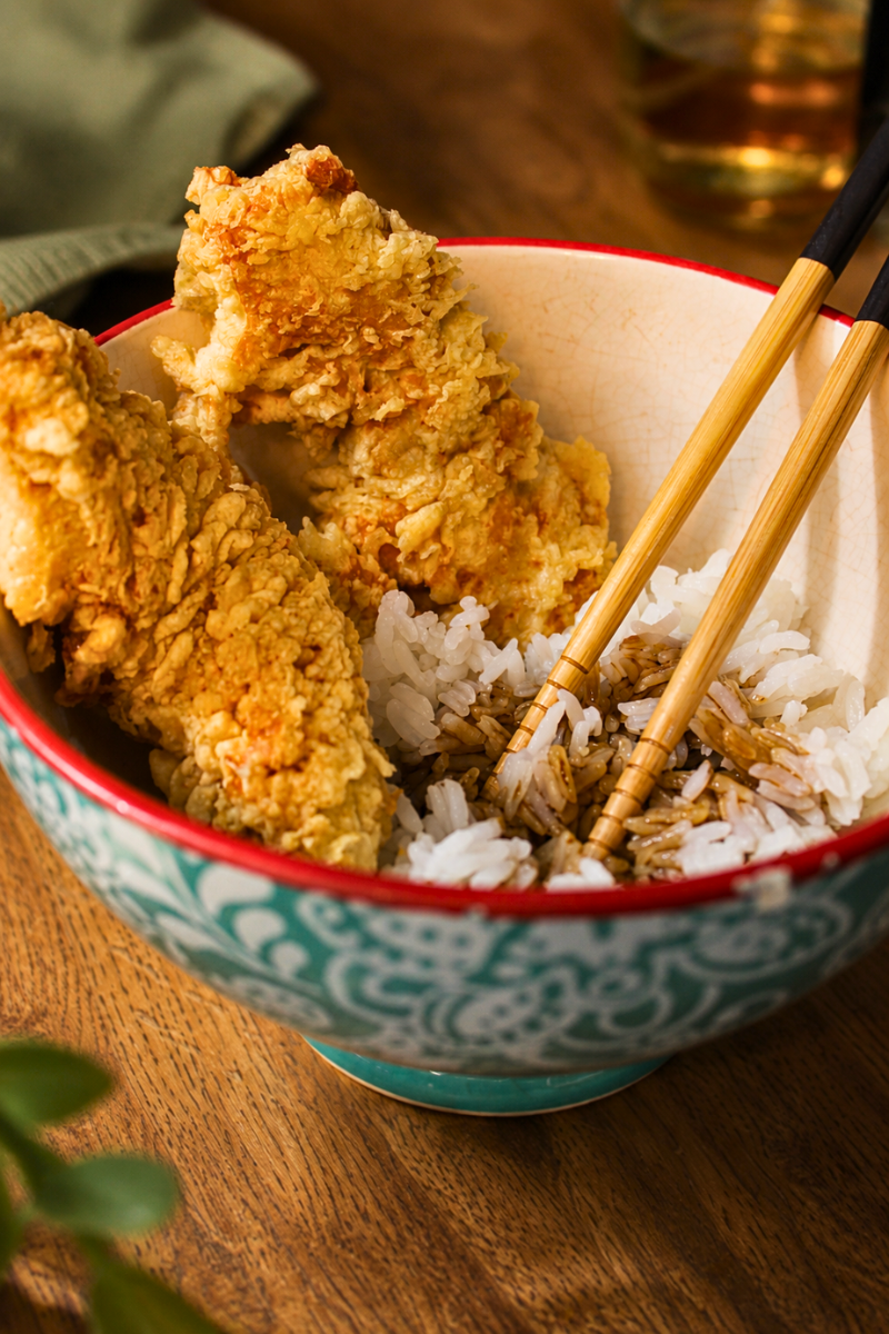 Close-up of crispy homemade Japanese chicken tempura served over steamed white rice in a decorative bowl with chopsticks and soy sauce, perfect for an authentic Japanese dinner recipe.
