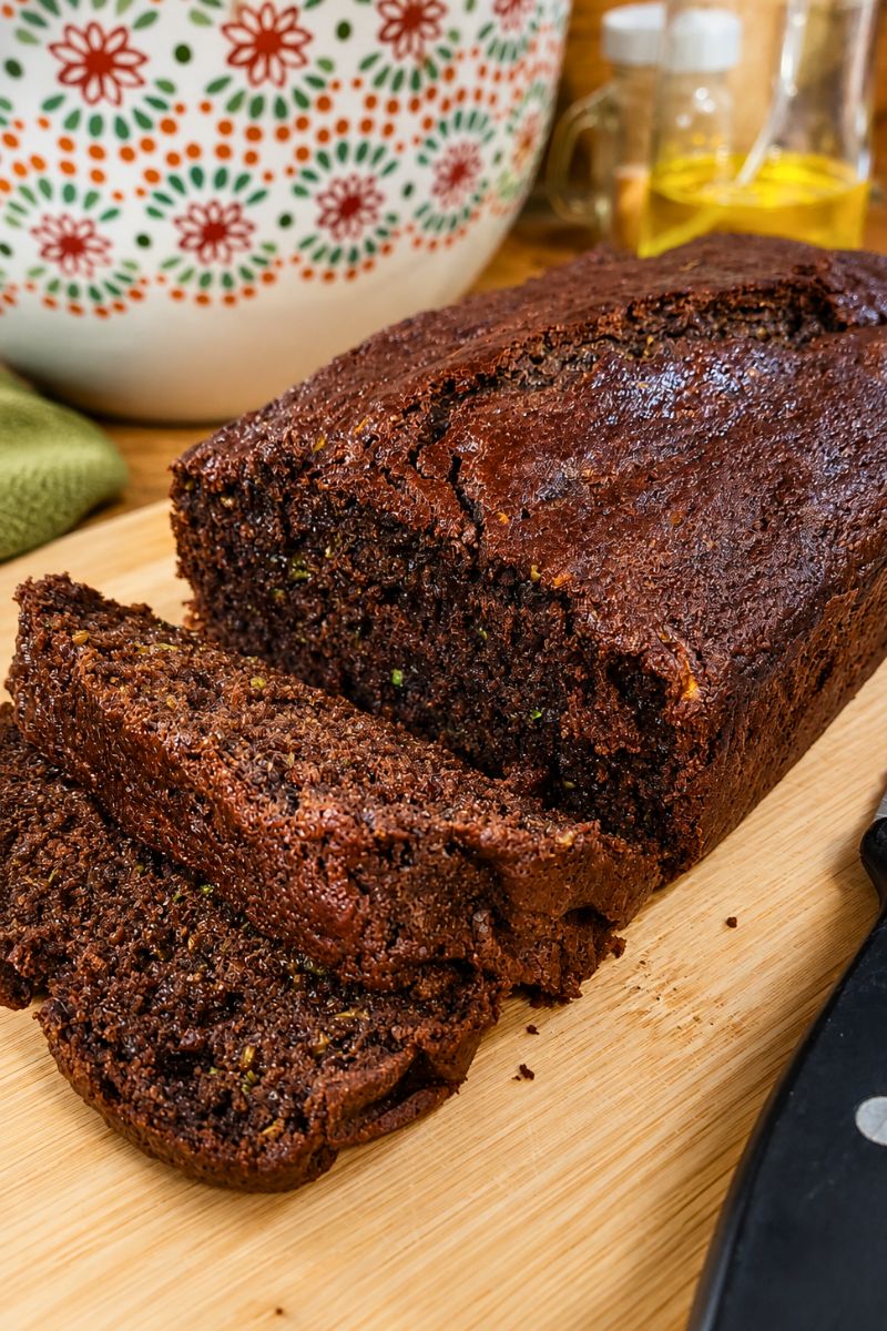 Honey-sweetened fresh-milled chocolate zucchini bread loaf with sliced pieces on a wooden cutting board.