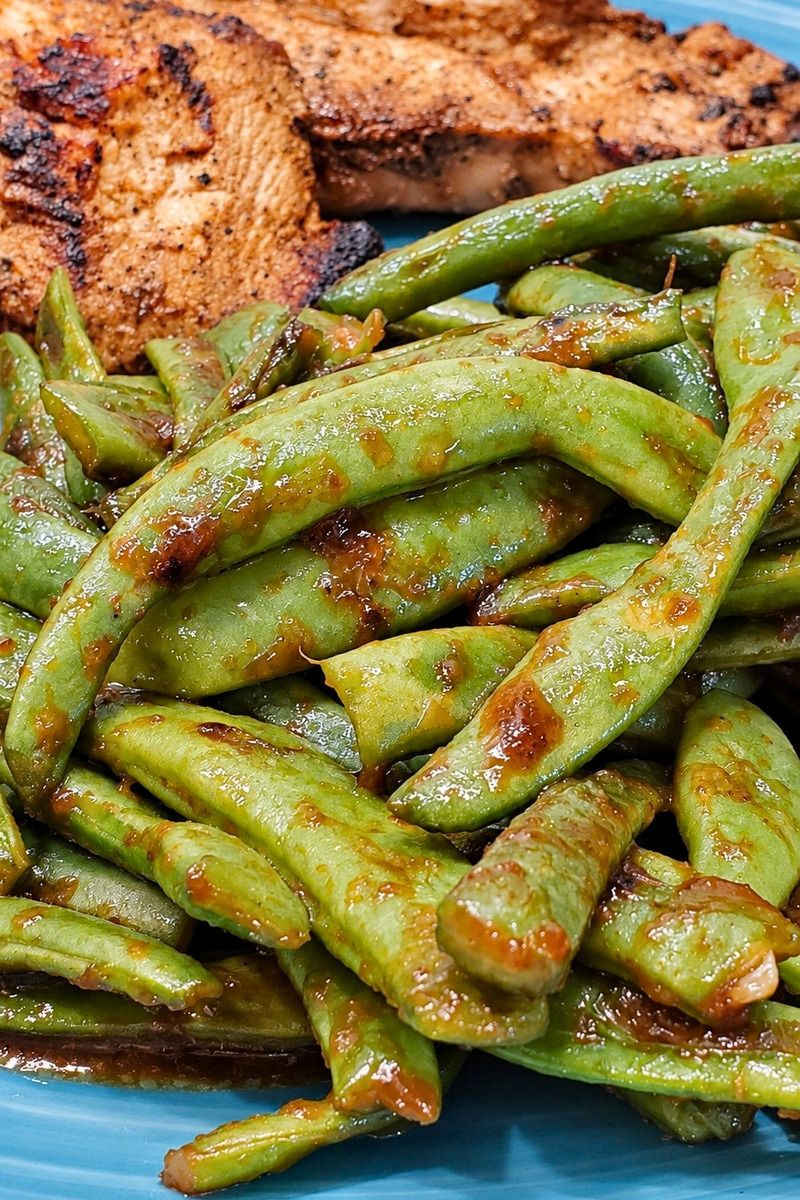 Close-up of Asian garlic green beans coated in a savory soy and oyster sauce glaze, served on a blue plate alongside pan-fried chicken.
