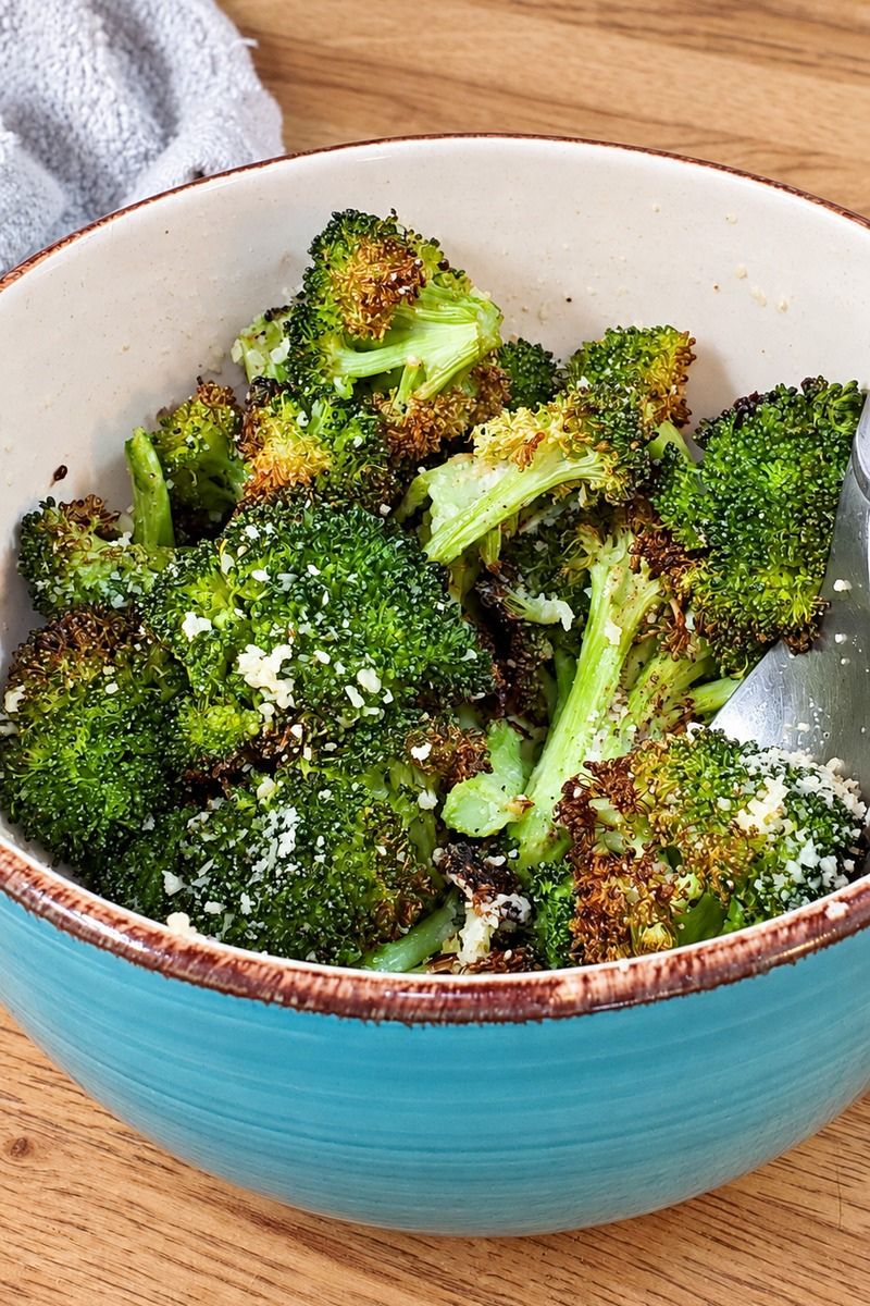 Roasted lemon garlic parmesan broccoli with crispy golden-brown edges and freshly grated parmesan cheese, served in a blue bowl for an easy, healthy oven-roasted broccoli side dish.
